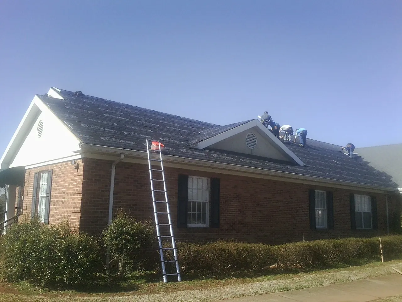 Crew tearing shingles off a brick ranch roof with a ladder set — Emergency Roof Repair work by our crew in Dufur
