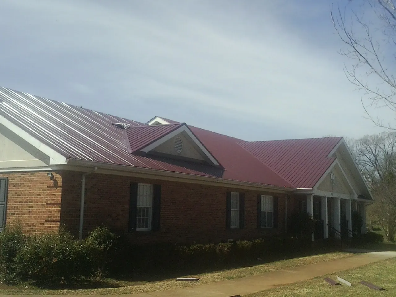 Red metal roof with gabled entries on a long brick building, from a Hail Damage Roof Repair job in Dufur