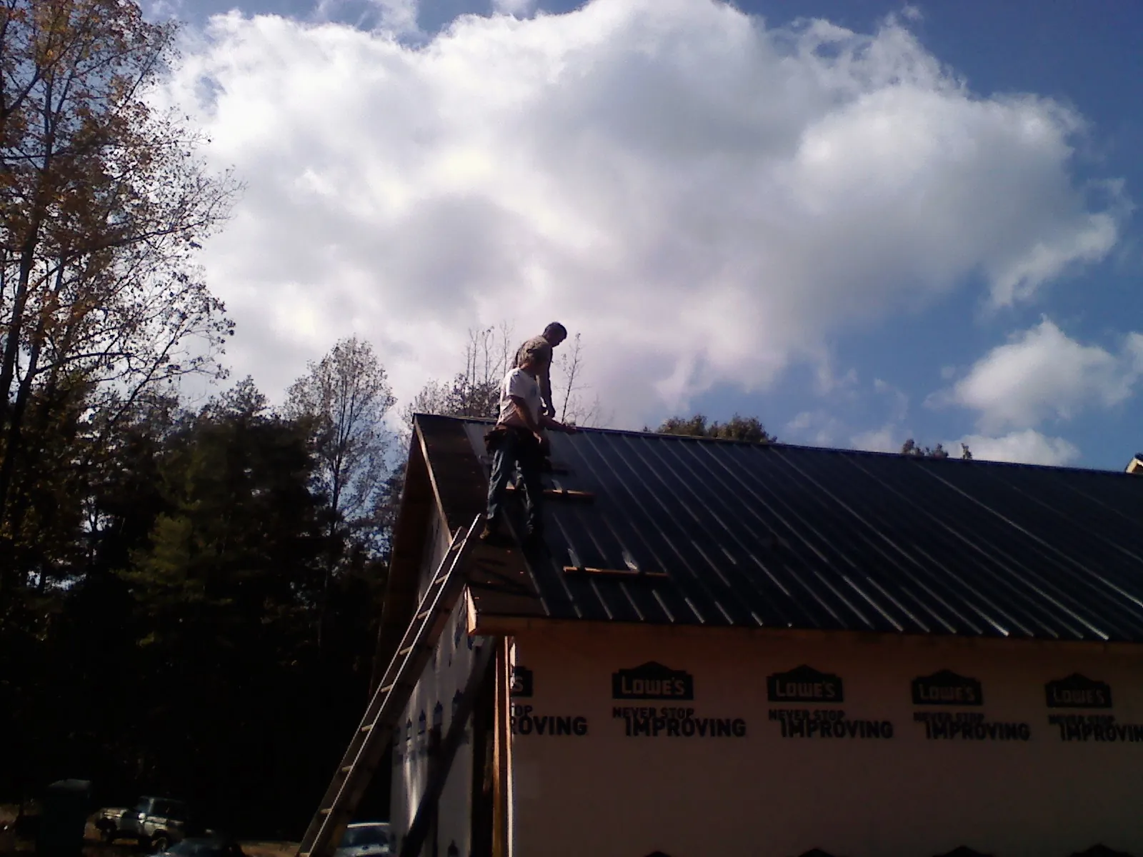 Roofer fastening dark metal panels high against a cloudy sky, from a Roof Inspection job in Dufur